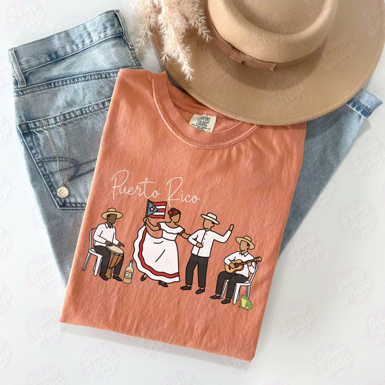 Pu&ograve; includere: Una maglietta color corallo con la scritta "Puerto Rico" e una grafica di persone che ballano e suonano strumenti. La maglietta &egrave; abbinata a jeans azzurri e un cappello color cammello.