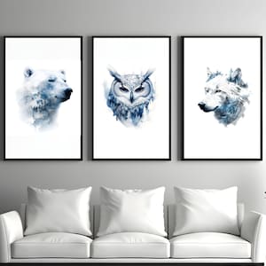 May include: Three framed art prints featuring watercolor illustrations of wildlife. The prints depict a polar bear, an owl, and a wolf, each rendered in shades of blue and white. The artwork is displayed above a white sofa.