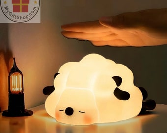 May include: A white sheep-shaped night light with black eyes and a mouth, illuminated and glowing, on a table top.