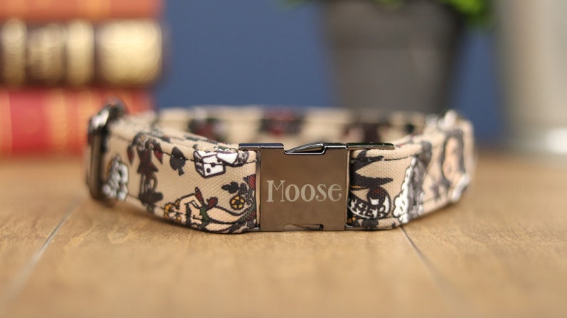 Op de afbeelding: Een tan hondenhalsband met een zwarte metalen gesp. De gesp heeft de naam "Moose" erop gegraveerd. De halsband is versierd met een tattoo-achtig patroon van speelkaarten, dobbelstenen en andere ontwerpen.