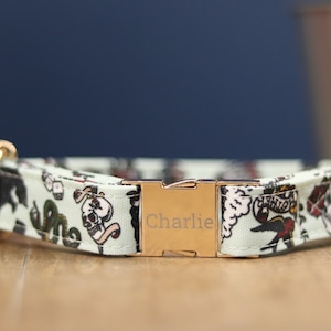 Peut inclure: Un collier de chien vert clair avec une boucle dorée. Le collier présente un motif inspiré des tatouages avec des crânes, des serpents et des dés. La boucle est gravée du nom "Charlie".
