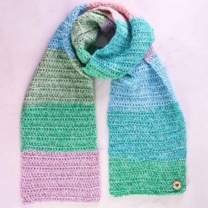 May include: A handmade crochet scarf in a gradient of colors, including blue, green, and pink. The scarf is made of soft yarn and features a textured stitch pattern. A wooden button with a heart detail is attached to one end.