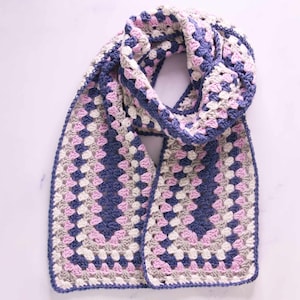 May include: A crocheted scarf in shades of pink, blue, and white. The scarf is made with a granny square pattern and has a fringed edge.