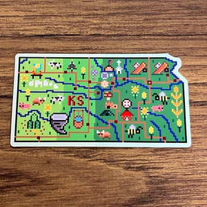 Pode incluir: Um mapa de Kansas em pixel art verde e azul com as letras "KS" no centro. O mapa está cheio de várias imagens de pixel art de animais de fazenda, plantações e outras imagens relacionadas ao Kansas.