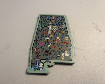 Può includere: Un adesivo verde e blu dello stato dell'Alabama con vari punti di riferimento e icone a pixel in tutto lo stato. L'adesivo ha la forma dello stato dell'Alabama.