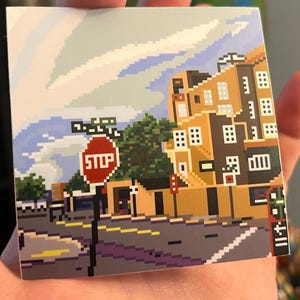May include: Pixel art illustration of a city street scene with a stop sign, a building with windows, and a blue sky with clouds. The street is paved with gray blocks and has yellow lines. The building is brown and yellow with a brown roof. The stop sign is red with white lettering that says "STOP".