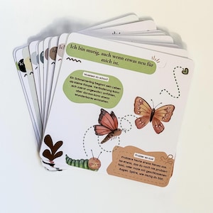 May include: A deck of illustrated cards with a nature theme. The cards feature images of butterflies, caterpillars, and leaves, along with German text. The cards are white with colorful illustrations and text in green, brown, and black.