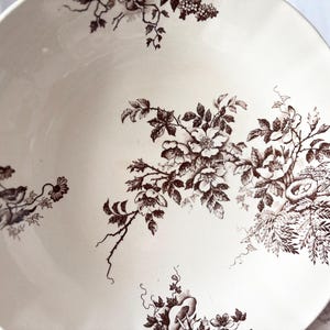 Pode incluir: Uma tigela de cer&acirc;mica branca com um padr&atilde;o floral castanho. A tigela apresenta um design delicado de rosas, folhas e p&aacute;ssaros. O padr&atilde;o lembra a porcelana vintage.