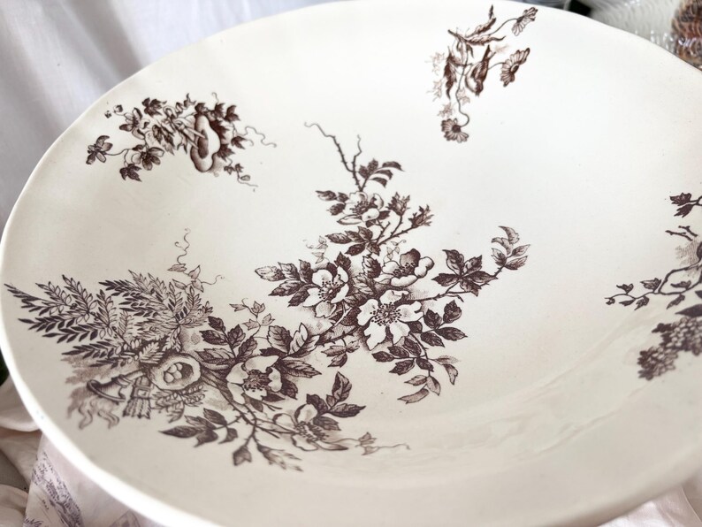 Pode incluir: Uma tigela de cer&acirc;mica branca com um padr&atilde;o floral castanho. A tigela apresenta um design delicado de rosas e folhas.