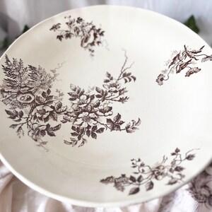 Pode incluir: Uma tigela de cer&acirc;mica branca com um padr&atilde;o floral castanho. A tigela tem uma borda larga e um po&ccedil;o profundo. O padr&atilde;o floral apresenta flores e folhas delicadas.