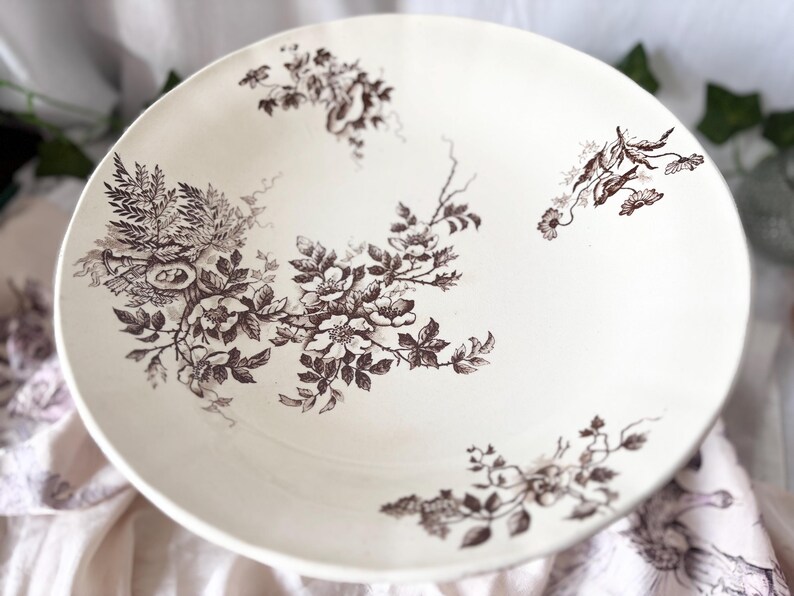 Pode incluir: Uma tigela de cer&acirc;mica branca com um padr&atilde;o floral castanho. A tigela tem uma borda larga e um po&ccedil;o profundo. O padr&atilde;o floral apresenta flores e folhas delicadas.