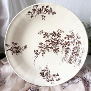 Pode incluir: Uma tigela grande de cer&acirc;mica branca com um padr&atilde;o floral castanho. A tigela apresenta um design delicado de flores, folhas e p&aacute;ssaros estilizados.