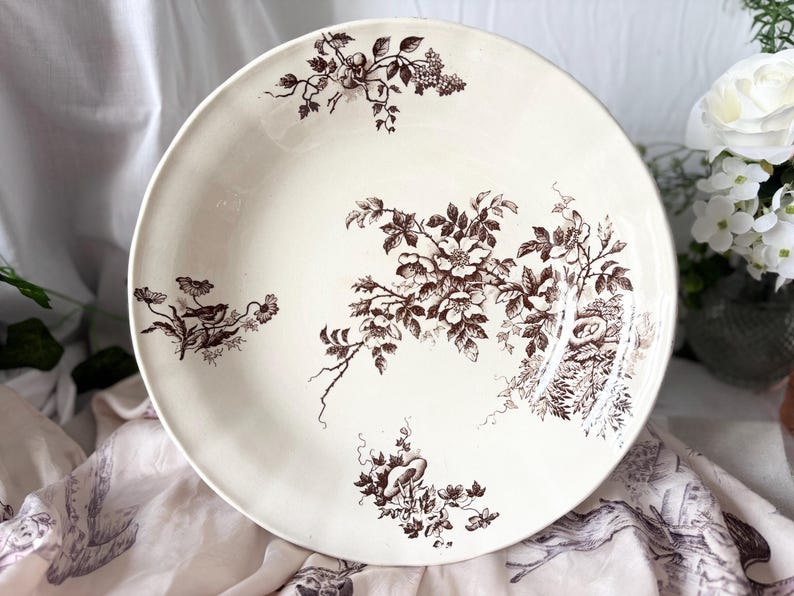 Pode incluir: Uma tigela grande de cer&acirc;mica branca com um padr&atilde;o floral castanho. A tigela apresenta um design delicado de flores, folhas e p&aacute;ssaros estilizados.