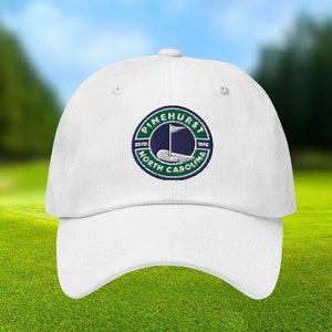 May include: White baseball cap with an embroidered green and blue logo that reads "Pinehurst, Est. 1901, North Carolina".