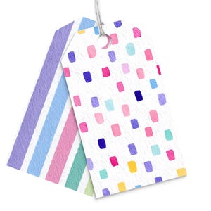 May include: Two gift tags with a watercolor design. One tag features vertical stripes in pastel colors, while the other has a white background with colorful rectangular shapes. Both tags are connected with a white string.