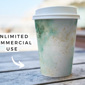 K&ouml;nnte beinhalten: Ein wei&szlig;er To-Go-Kaffeebecher mit einem gr&uuml;nen und goldenen Aquarelldesign. Der Becher steht auf einem Holztisch. Der Text "UNLIMITED COMMERCIAL USE" ist im Bild sichtbar.