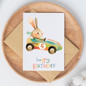 May include: A birthday card featuring a cartoon bunny driving a toy race car with the number 4 on the side. The card has the text "happy birthday" in colorful letters.