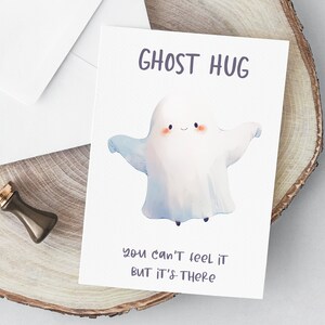 May include: A white ghost with a smiling face and outstretched arms, with the text "GHOST HUG" above and "you can't feel it but it's there" below.
