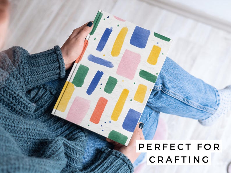 May include: A notebook with a white cover featuring colorful brushstroke designs in blue, yellow, green, pink, and orange. The text "PERFECT FOR CRAFTING" is visible on the bottom right.