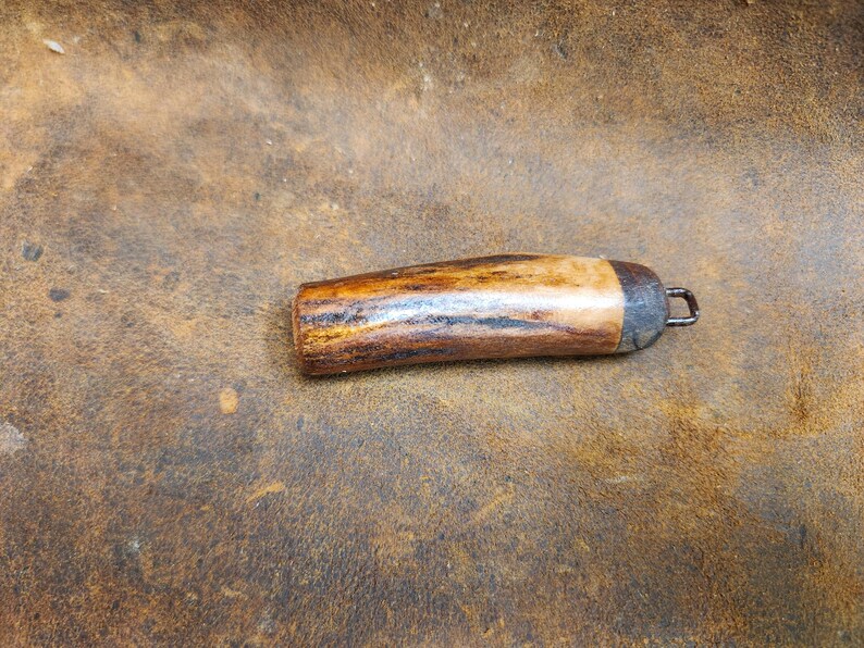 May include: A handcrafted, wooden bottle stopper with a natural, warm-toned finish. The stopper features a dark metal cap and a small metal loop for easy removal. The wood grain is visible, adding to its rustic charm.