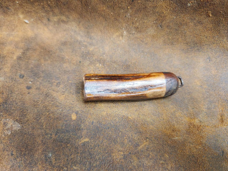 May include: A cylindrical bottle stopper made of wood and metal. The wooden portion has a light brown and dark brown pattern, with a silver-colored metal cap and a small loop for attachment. The stopper is designed to fit into a bottle.