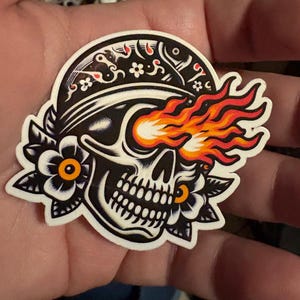 May include: A black and white skull with a bandana and one eye on fire. The skull is surrounded by black and white flowers.