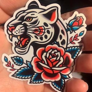 Puede incluir: Un pantera blanco y negro con una rosa roja y hojas azules y verdes. La pantera tiene una expresión feroz y mira hacia la izquierda. La rosa está en plena floración y tiene un centro blanco.