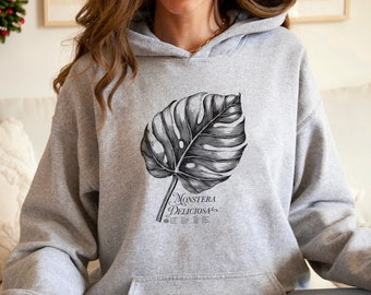 May include: A gray hooded sweatshirt with a black and white illustration of a Monstera Deliciosa leaf. The text "Monstera Deliciosa" is printed below the leaf.