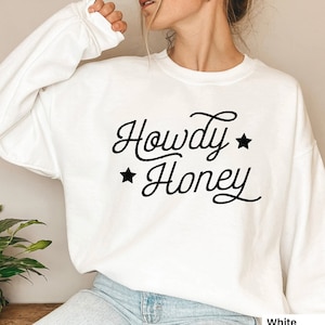 May include: White sweatshirt with the text "Howdy Honey" in black cursive lettering with two black stars on either side of the text.