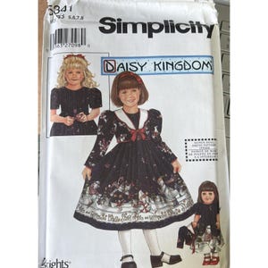 May include: Simplicity sewing pattern for a Daisy Kingdom dress. The pattern features a black dress with a white collar and a red bow. The dress has a print of snowmen and the text "Starry Nights and Peppermint Bites".
