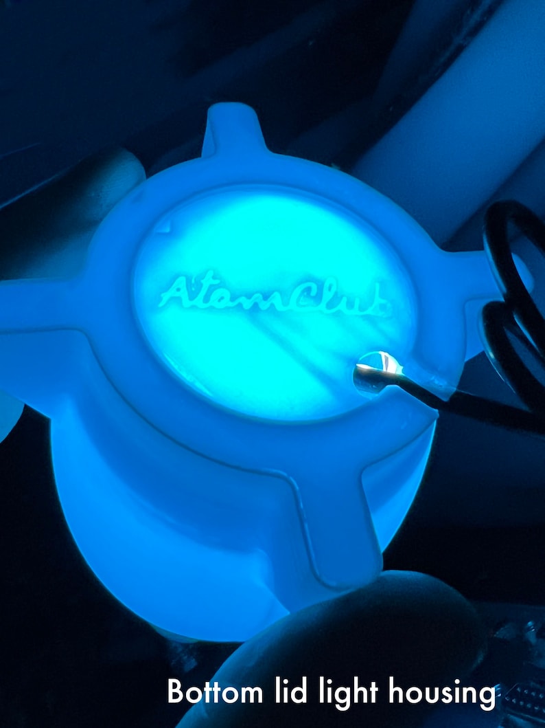 May include: A blue plastic light housing with the text "Atom Club" printed on the top. The housing is designed to fit on the bottom lid of a product.