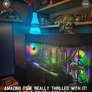 May include: A black computer case with a clear side panel, showcasing colorful RGB fans and a graphics card. The case is lit with blue and green lights. The text "GEFORCE RTX" is visible on the graphics card.