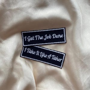 May include: Two black embroidered iron-on patches with white text. The top patch reads "I Get The Job Done". The bottom patch reads "I Take It Like A Taker".