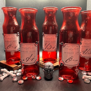 May include: Five red glass bottles with labels reading "Bloody Bert", "Bloody Mary", "Bloody Kate", "Bloody Ann", and "Bloody Tom". A small skull, bone decorations, and red and clear glass beads are also present.