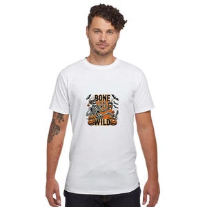 May include: White t-shirt with a graphic of a skeleton sitting on pumpkins and the text "Bone to be Wild".