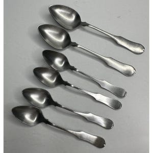 May include: Six antique silver spoons arranged diagonally. Each spoon has an oval bowl and a long, slender handle with a decorative design near the bowl. The spoons are made of a shiny, reflective metal, likely silver or a silver alloy.