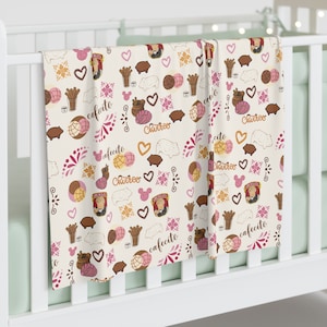 May include: A white cot sheet with a repeating pattern of pink hearts, brown pigs, and illustrations of Mexican pastries, including conchas, churros, and cafe con leche. The text "cafetito", "churro", and "afecto" is repeated throughout the pattern.