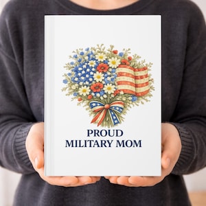 May include: A white notebook held by a person, featuring a floral bouquet with an American flag design. The bouquet includes blue, red, and white flowers, and a ribbon with stars and stripes. The text "PROUD MILITARY MOM" is below the floral design.