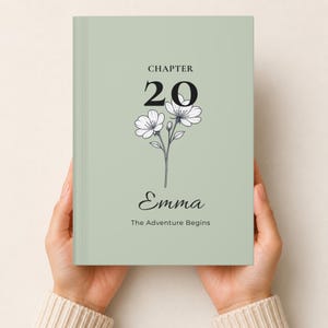May include: A sage green hardcover book featuring the text CHAPTER 20, a black line drawing of two flowers, the name Emma in a script font, and the text The Adventure Begins printed in black on the front cover.