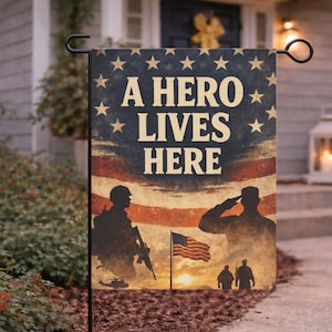 May include: A patriotic garden flag with the text "A HERO LIVES HERE" against a backdrop of the American flag and silhouettes of soldiers. The flag features a sunset scene and a waving American flag.