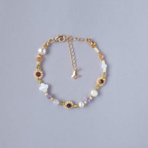 Peut inclure: Un bracelet de perles délicat avec un mélange de perles colorées, dont des perles, des accents violets et dorés. Le bracelet comprend de petites perles en forme de fleur et de trèfle, et un fermoir doré avec un petit charme.