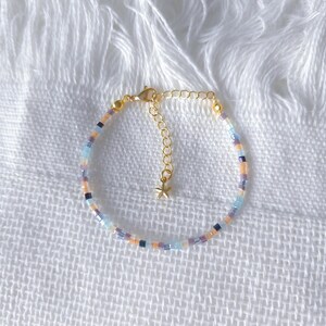 May include: A delicate beaded bracelet with a gold-coloured chain and clasp. The bracelet features small, colourful beads in shades of blue, purple, orange, and black. A small gold star charm hangs near the clasp.