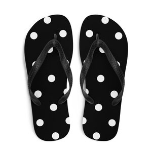 May include: A pair of black flip-flops with a white polka dot pattern. The straps are black. These sandals are perfect for casual wear and beach outings.