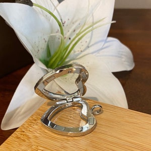 Puede incluir: Un medall&oacute;n de plata en forma de coraz&oacute;n con una ventana de vidrio transparente. El medall&oacute;n est&aacute; abierto y el interior es visible. El medall&oacute;n est&aacute; sobre una superficie de madera.