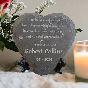 May include: A grey heart-shaped slate plaque with a memorial message engraved on it. The message reads: "May the winds of heaven blow softly and whisper in your ear how much we love and miss you and wish that you were here." The plaque also includes the name "Robert Collins" and the dates "1951-2024".