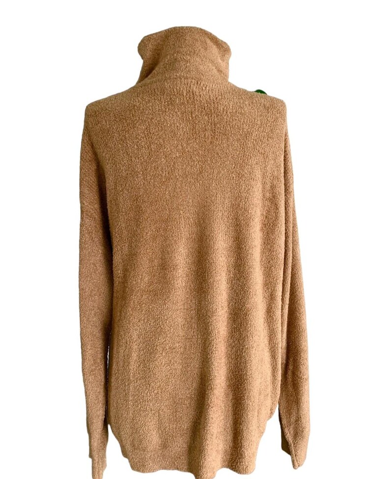May include: A tan-coloured turtleneck jumper with long sleeves. The jumper has a soft, textured appearance and a relaxed fit. The turtleneck is folded over. The jumper is made of a warm, comfortable material.