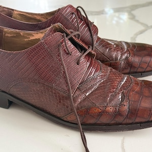 Peut inclure: Une paire de chaussures richelieu en cuir marron avec un motif texturé façon lézard sur le quartier et un motif gaufré façon crocodile sur le bout et l'empeigne. Les chaussures comprennent des lacets marron foncé et un petit talon.
