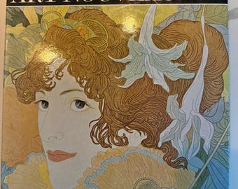 May include: A book titled Art Nouveau from The Colour Library of Art featuring 54 full colour illustrations. The cover displays a detailed portrait of a person with wavy auburn hair, adorned with white lily flowers, set against a yellow background.