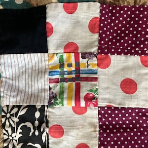 Może przedstawiać: Kołdra patchworkowa z kwadratami z różnych tkanin. Tkaniny obejmują czarny, biały, czerwony, brązowy i zielony. Niektóre kwadraty mają wzór w kropki, podczas gdy inne mają paski lub wzory kwiatowe.