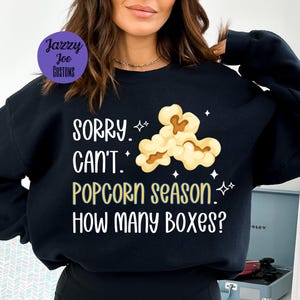 May include: Black sweatshirt with a white graphic that says "SORRY. CAN'T. POPCORN SEASON. HOW MANY BOXES?" and a cartoon image of popcorn.